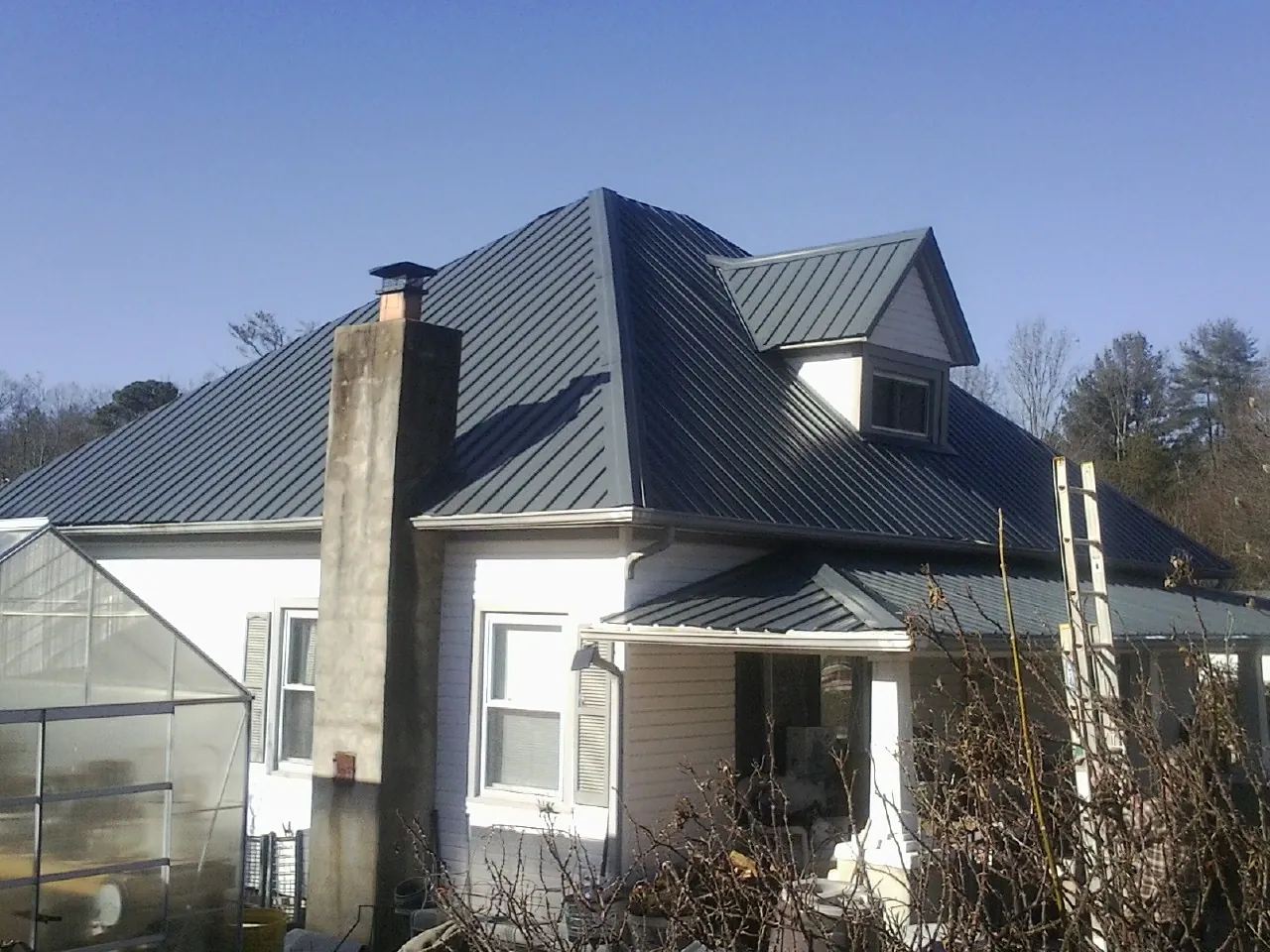 Dark blue standing seam metal roof on a white farmhouse with dormer — Slate & Tile Roof Repair by Roofing Brothers in Mc Coll