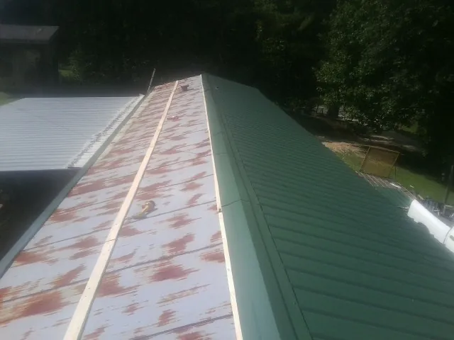 Old rusted panels beside newly installed green metal roofing — Wind Damage Roof Repair by Roofing Brothers in Mc Coll