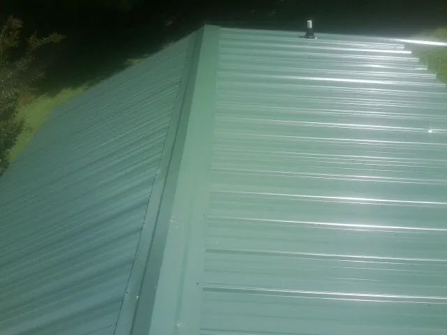 New green metal panels meeting at the ridge of a roof — Flat Roof Repair work by our crew in Mc Coll