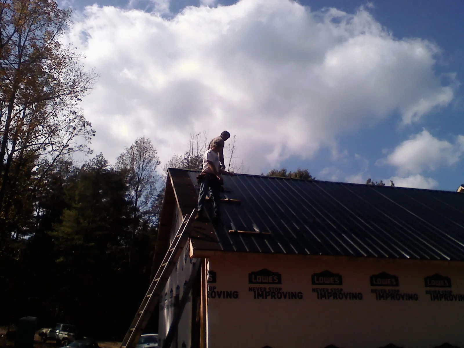 Roofer fastening dark metal panels high against a cloudy sky, from a Roof Inspection job in Mc Coll