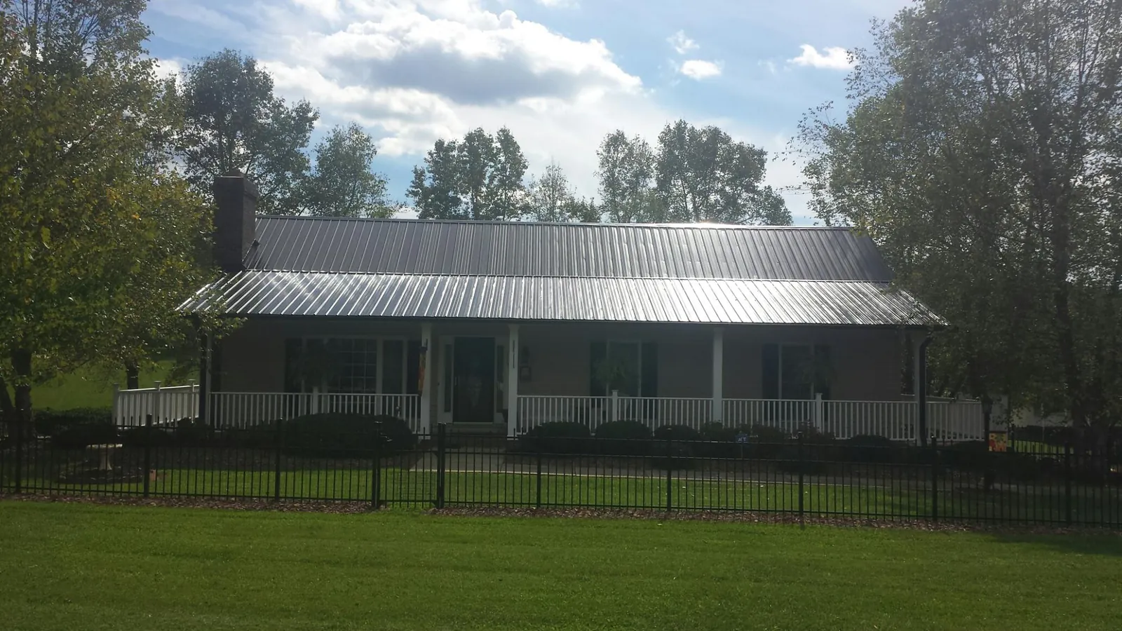Gray metal roof on a brick ranch with a full width front porch — Gutter Guard Installation work by our crew in Mc Coll