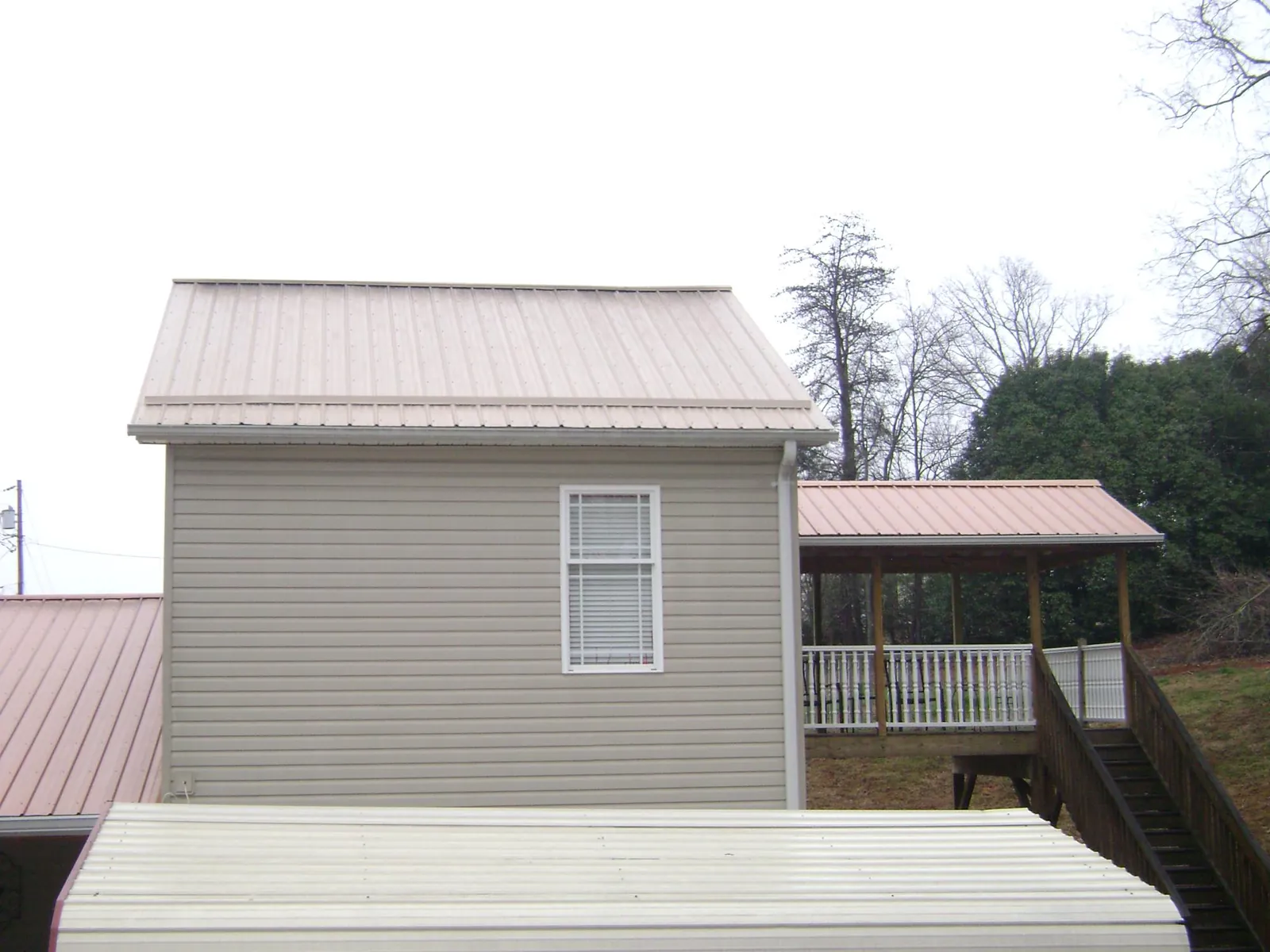 Tan metal roofs on a two story addition and attached porch, from a Roof Replacement job in Mc Coll